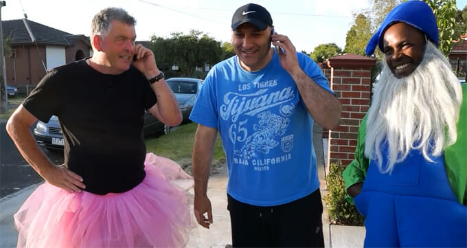 Three men in tutu costumes talking on the phone while greeting each other.