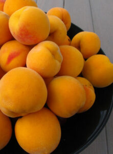 A bowl full of Prunus 'Golden Queen' Peach (Dwarf) Bare Rooted on a wooden table.