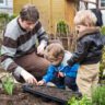 A man and two children celebrate Father's Day in a garden, surrounded by a variety of plants.