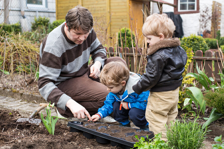 A man and two children celebrate Father's Day in a garden, surrounded by a variety of plants.