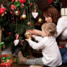 A mother and child joyously adorning a Christmas tree with festive ornaments and lights.