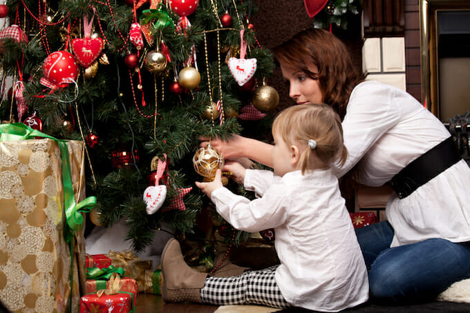 A mother and child joyously adorning a Christmas tree with festive ornaments and lights.
