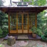 Wooden Tea House cabin with large glass doors surrounded by lush greenery.