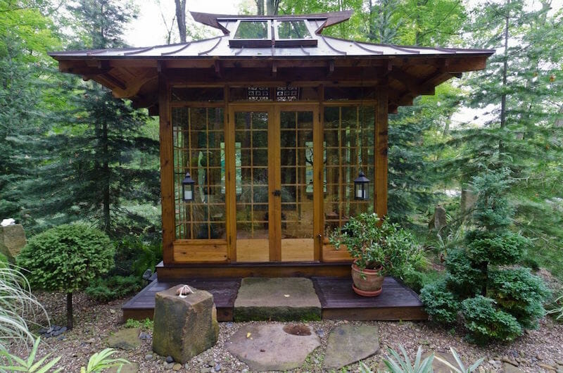 Wooden Tea House cabin with large glass doors surrounded by lush greenery.