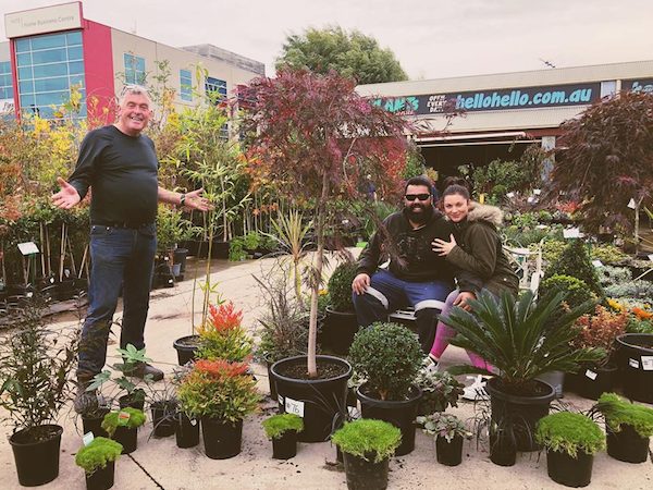 A group of three people sharing customer stories amongst various potted plants at a garden center.