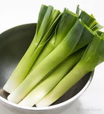 A bowl containing fresh leeks with vibrant green tops and white stems, displayed in a Leek 3" Pot set against a white background.
