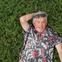 Man lying on the grass, smiling at the camera with a Myoporum 'Broad Leaf' 6" Pot (Bulk Buy 12) beside him.