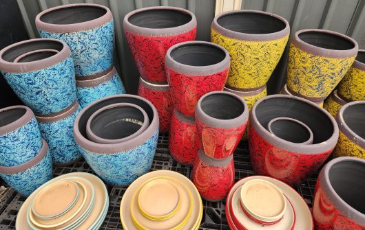 A variety of Tang Rustica Tall Planter Yellow with Saucer S 24x29cm pots and plates are sitting on a rack.