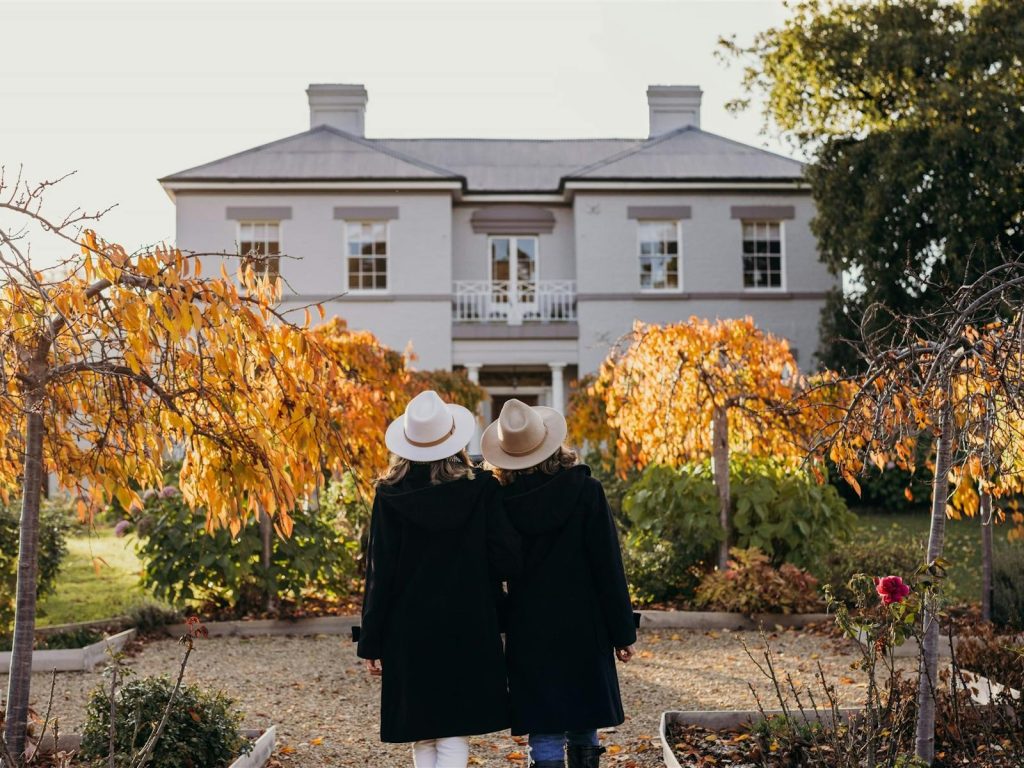 Two women walking in front of a house in autumn.