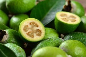 Fresh feijoas (pineapple guavas) with one cut in half, revealing the flesh and seeds, on a wooden surface. feijoa acca