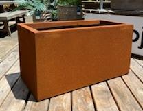 A rectangular corten steel Brighton Trough Rust L planter box, 100x46x46cm, on a wooden deck.