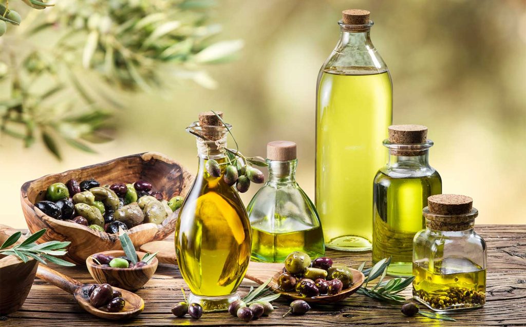 Various bottles of olive oil and a selection of green and black olives with olive branches, evoking the essence of a planting garden, on a wooden table. Olive oil