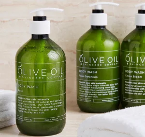 Three bottles of olive oil body wash from olive oil skincare company, displayed on a marble countertop.