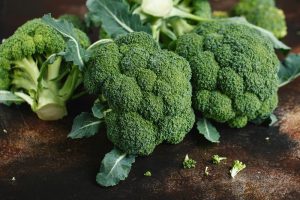 Fresh broccoli heads with leaves are displayed on a dark countertop, alongside the intricate, emerald-green spirals of Broccoli 'Romanesco' (Copy).