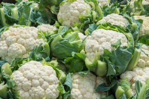 A pile of fresh cauliflower heads with green leaves.