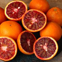 A 4L Citrus ‘Arnold’ Blood Orange sits on a wooden surface, its vibrant red and orange flesh displayed—perfect for refreshing recipes.