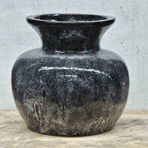 A large, glossy black ceramic vase with a wide body and narrow neck sits on a light wooden surface against a gray background.